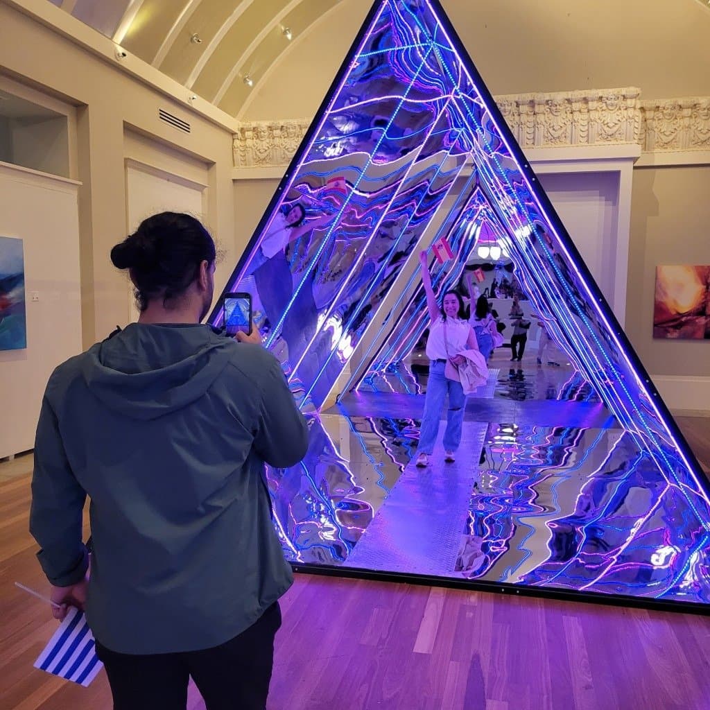 Visitors photographing each other inside the mirror pyramid installation at The Coliseum of Art